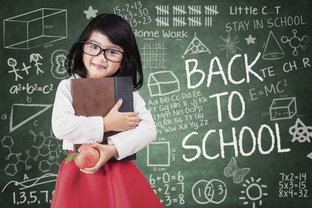 42870115 - little girl holds a book and apple back to school in classroom