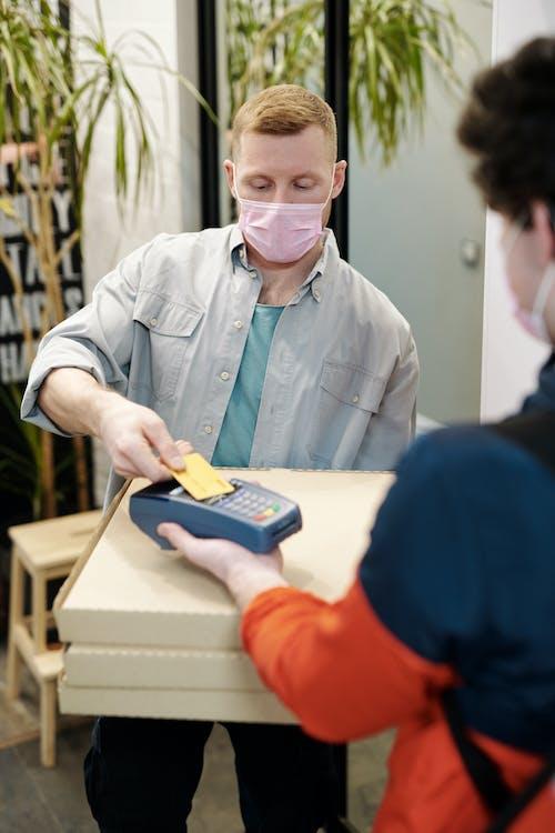 A person wearing a mask paying for pizza using a credit card