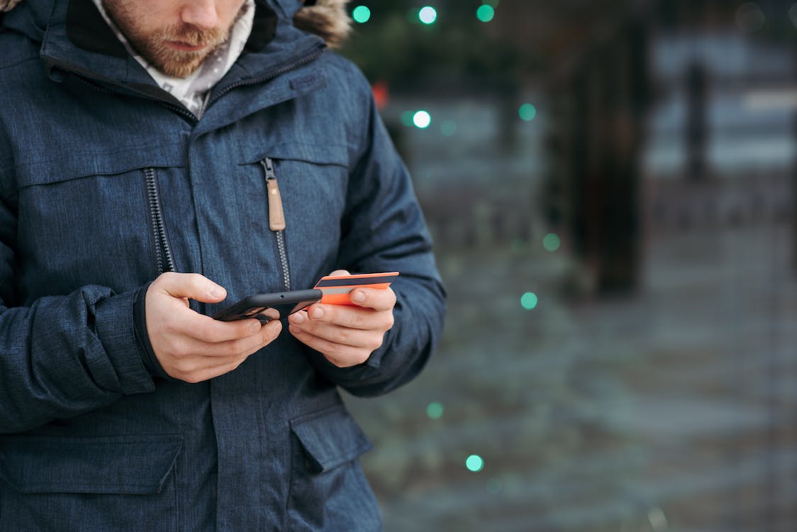 Man browsing smartphone and holding credit card on the street
