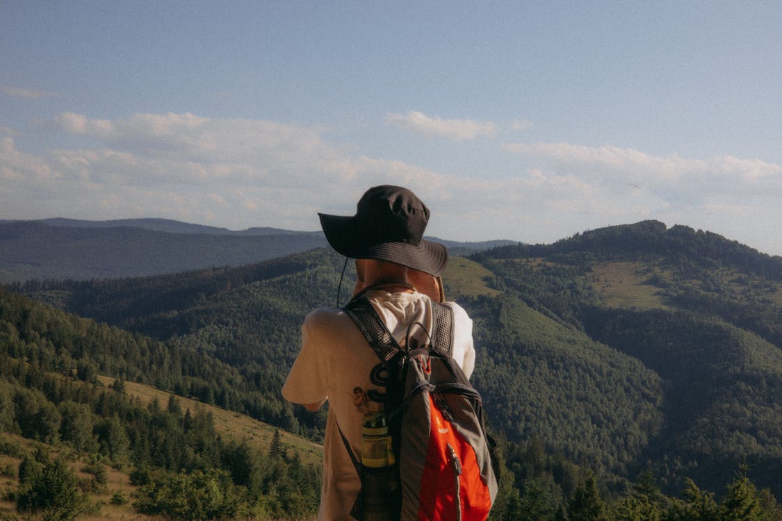 man in a hat and with a backpack standing with hills behind