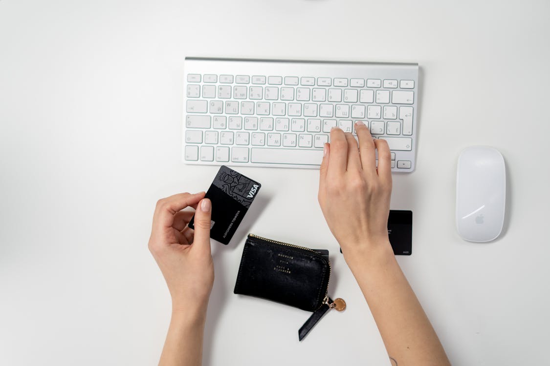 person typing on a keyboard while holding a credit card on the other hand