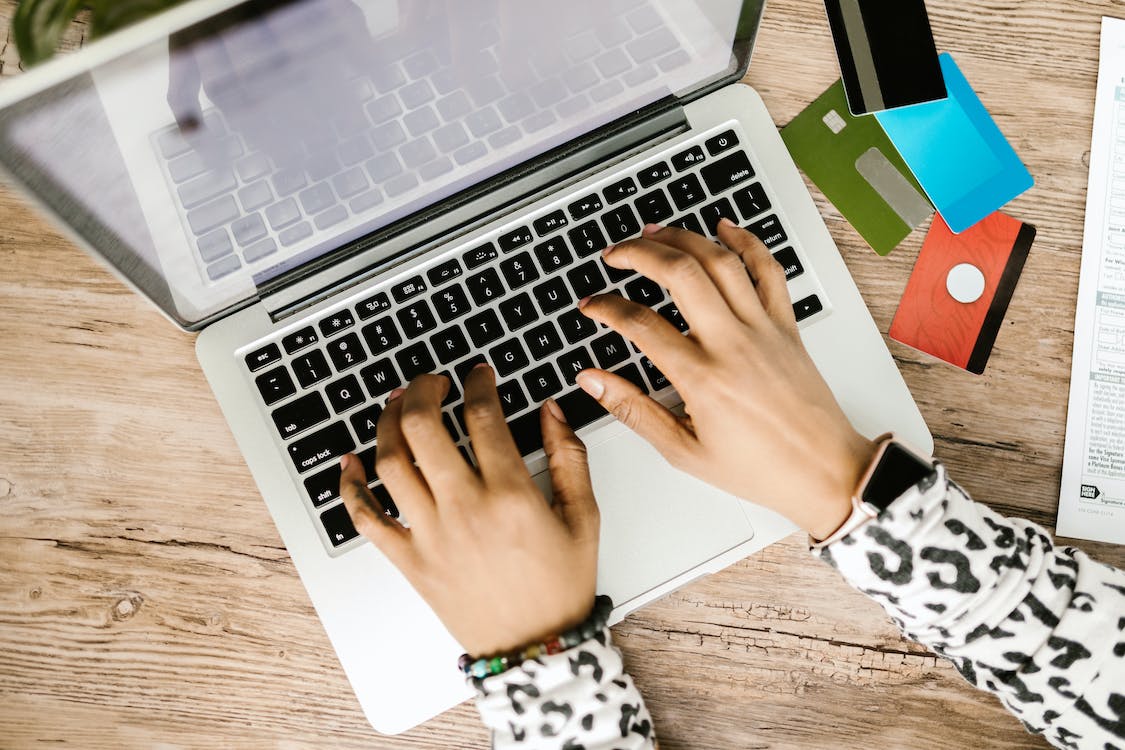 a person typing on a laptop with several credit cards beside it