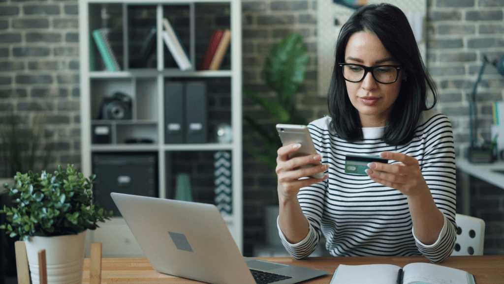 Woman checking her credit card and phone while reviewing payments to lower statement date utilization in Canada